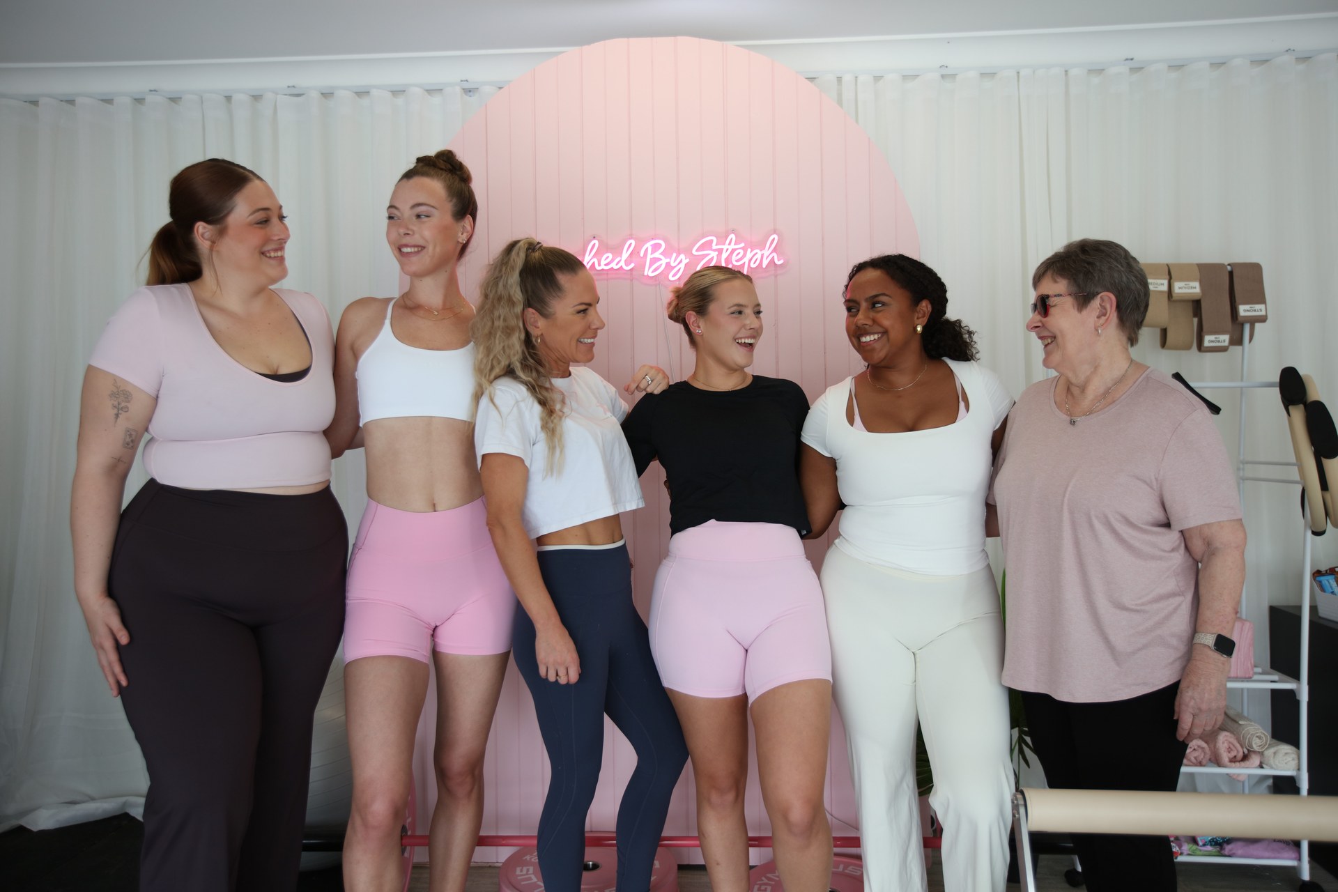 Steph and a group of women together in her private studio, in front of the pink arch